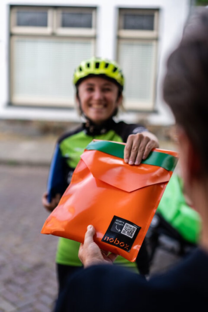 Fietskoerier overhandigt een oranje Nobox-verzendhoes aan de ontvanger